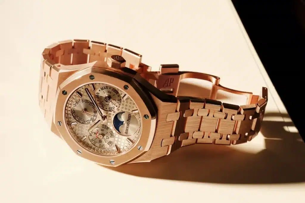 A luxurious gold watch with a detailed face showing a moon phase indicator and multiple dials, featuring a link bracelet and an engraved clasp.