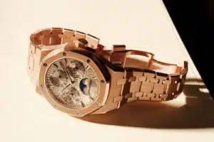A luxurious gold watch with a detailed face showing a moon phase indicator and multiple dials, featuring a link bracelet and an engraved clasp.