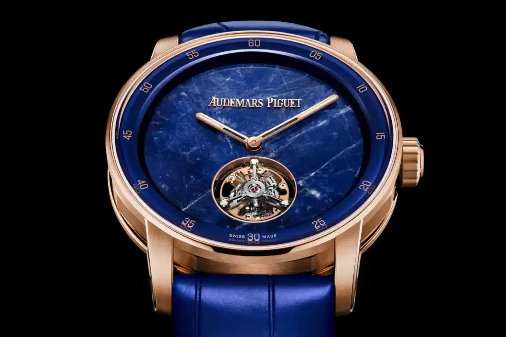 A luxury watch with a blue watch face featuring a visible tourbillon mechanism and rose gold hands and accents, marked with the brand name 'Audemars Piguet.' The watch has a blue leather strap and rose gold casing. Audemars Piguet - 150th Anniversary Special Editions