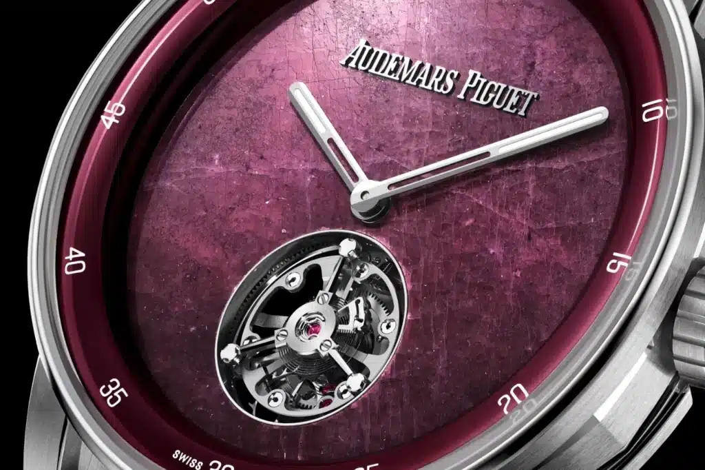 Close-up view of a luxury watch featuring a textured purple dial, with thin silver hour and minute hands, and the brand name "Audemars Piguet" inscribed at the top. The watch includes a visible tourbillon mechanism at the 6 o'clock position, showcasing intricate mechanical details.