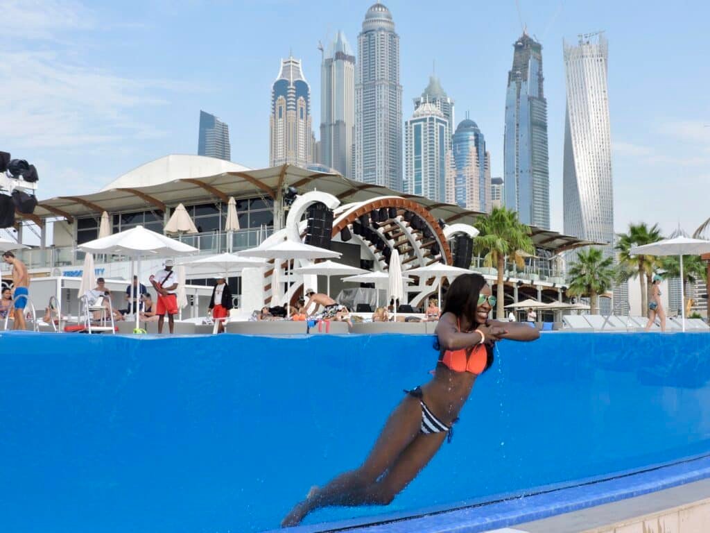 A woman in a bikini leaning over the edge of an infinity pool with a city skyline in the background at Zero Gravity Dubai.
