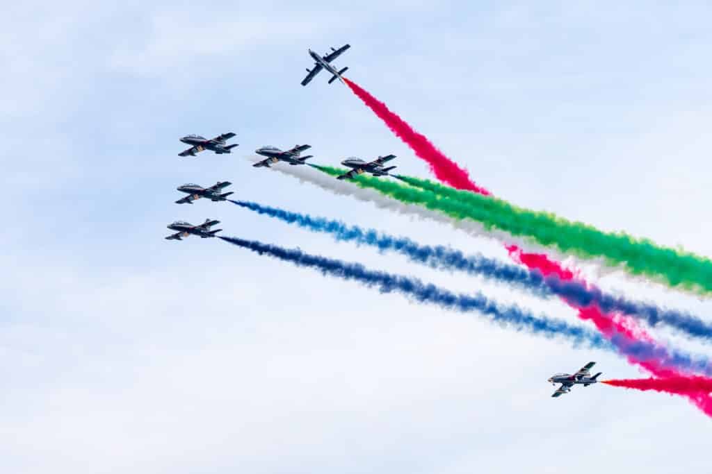 A formation of seven jets flying in the sky, emitting trails of colored smoke in red, green, blue, and white. Eid Al Etihad 2025 Celebrations.