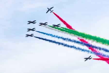 A formation of seven jets flying in the sky, emitting trails of colored smoke in red, green, blue, and white. Eid Al Etihad 2025 Celebrations.