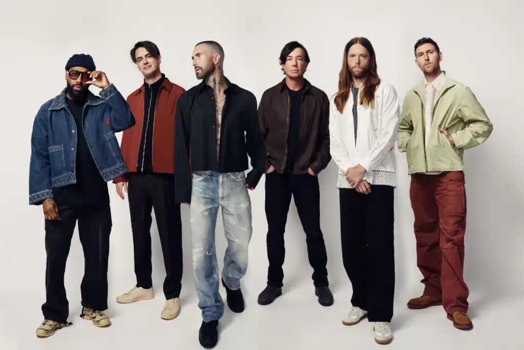 A group of six men standing side by side, each wearing different casual and stylish clothing, against a plain background. Upcoming Concerts.