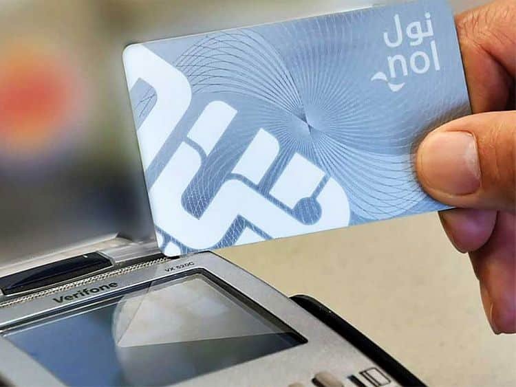A hand holding a Dubai Nol card near a Verifone payment terminal's screen, indicating a contactless payment or transaction.
