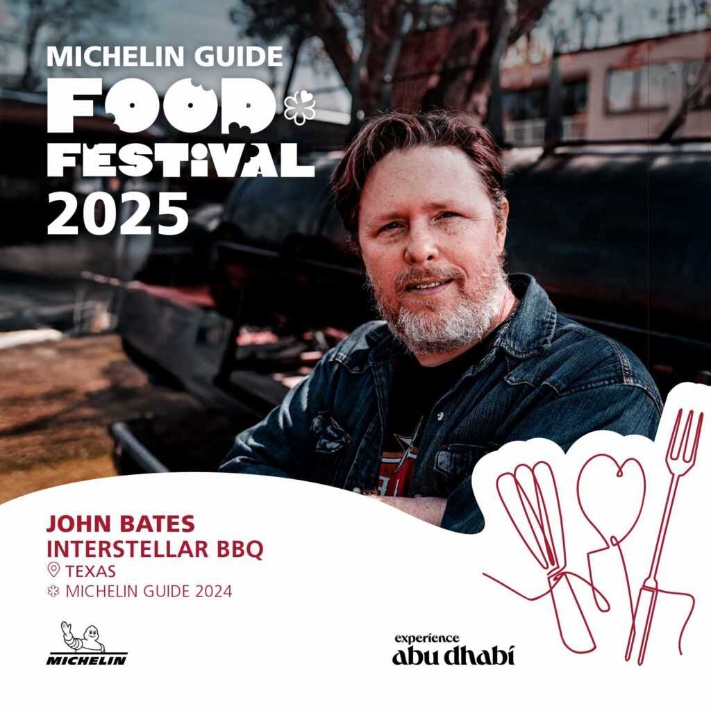 A man with a beard and wearing a denim jacket stands in front of a barbecue setup. The image promotes the Michelin Guide Food Festival 2025, featuring John Bates from Interstellar BBQ in Texas, highlighted in the Michelin Guide 2024. Logos of Michelin and Experience Abu Dhabi are also visible.