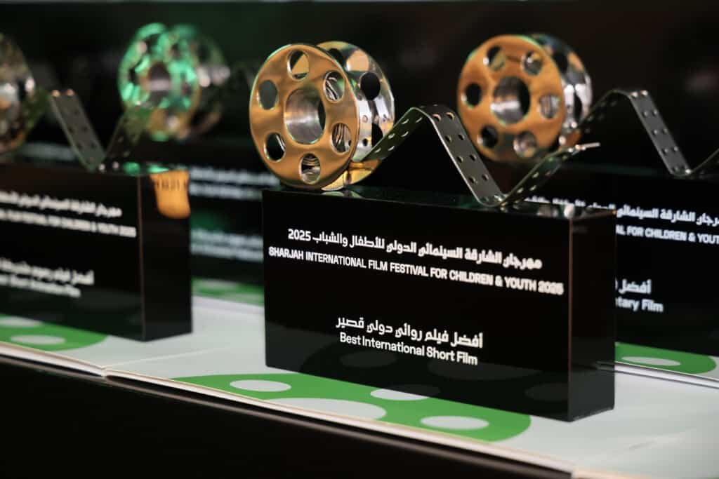 Close-up of awards for the Sharjah International Film Festival for Children & Youth 2025, featuring a golden film reel design on a black base with inscriptions recognizing "Best International Short Film."