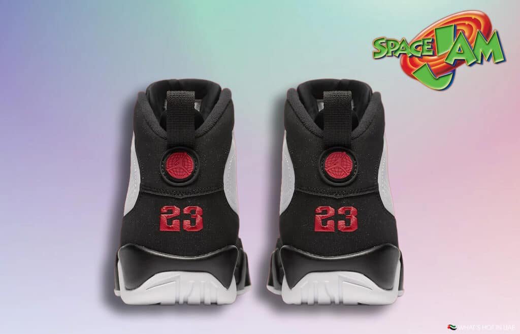 A pair of black and white sneakers viewed from the back, with a red number '23' embroidered on the heel and a red circular logo above. The background features a pastel gradient and a 'Space Jam' logo in the top right corner.