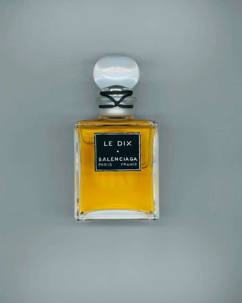 A bottle of Le Dix perfume by Balenciaga, featuring a clear glass rectangular design filled with amber liquid and a round stopper, labeled with "Le Dix" and "Balenciaga Paris France." part of the Balenciaga fragrance collection.