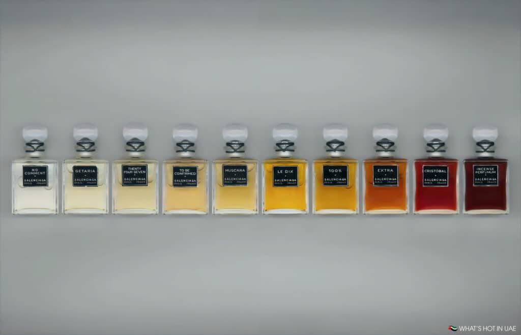 A row of eleven Balenciaga perfume bottles, each with a distinct label and color, arranged against a neutral background.