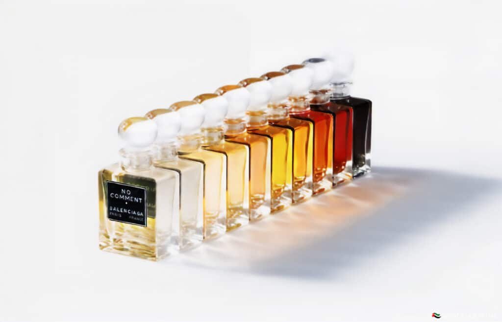 A row of elegant perfume bottles with varying shades of liquid, arranged in a gradient from light to dark, featuring a label that reads "No Comment Balenciaga Paris France."
