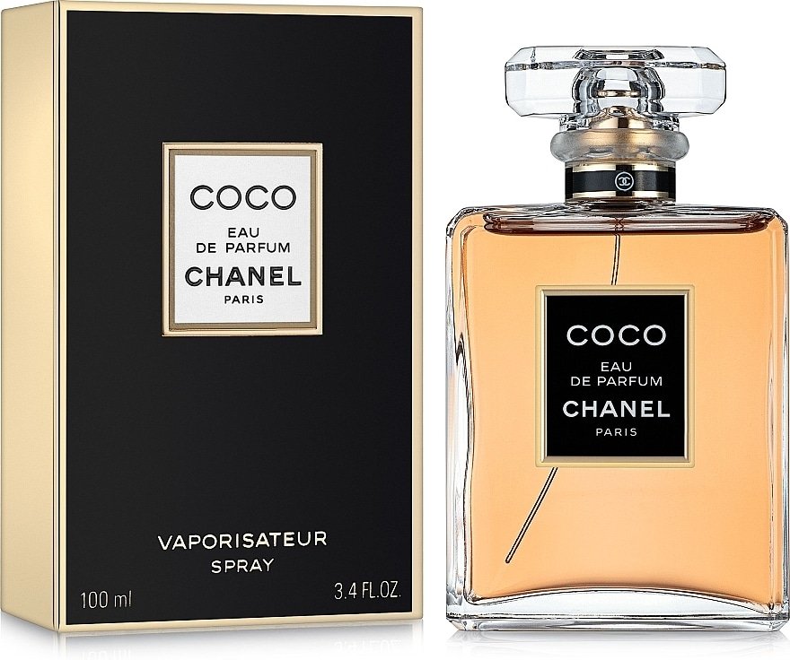A bottle and box of Coco Eau de Parfum by Chanel. The bottle is transparent with a black and gold label and a clear cap, holding an amber-colored liquid. The box is black with a similar gold-bordered black label.