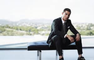 A man in a suit sits on a modern bench in front of a large window with a blurred outdoor view.