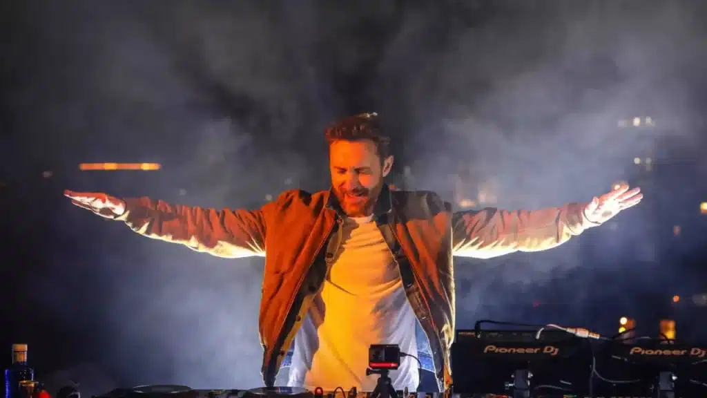 David Guetta Ushuaia Dubai performing live on stage, with arms outstretched and a smile, surrounded by fog and lights.
