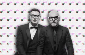 Two men in black suits and glasses stand in front of a backdrop with repeated text "WHAT'S HOT IN UAE" and images of the UAE flag.