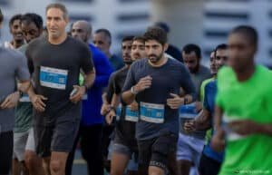 A group of runners participating in a marathon, wearing athletic clothing and numbered bibs, with two men in dark shirts prominently visible at the front.