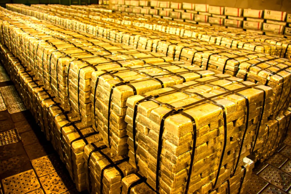 Large stacks of gold bars wrapped in black straps arranged in a warehouse.