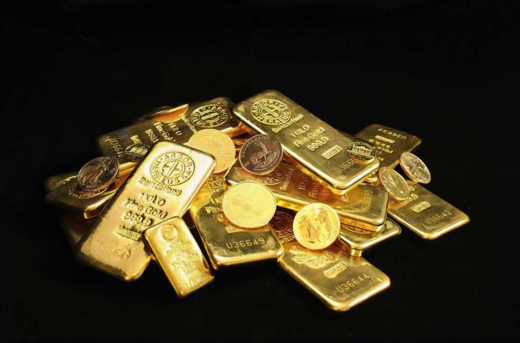 A pile of gold bars and gold coins on a dark surface, with the bars marked as 999.9 fine gold from Switzerland.