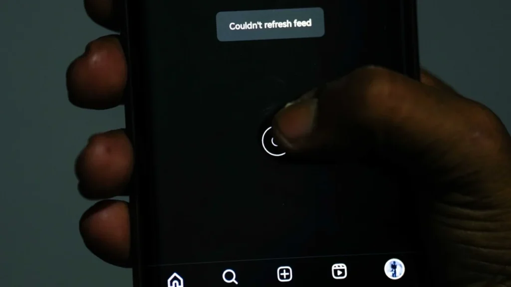 Close-up of a smartphone screen displaying the message "Couldn't refresh feed," with a hand touching the screen and icons visible at the bottom.