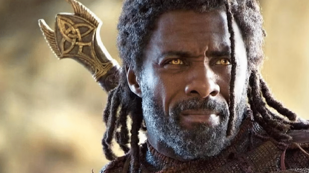 Idris Elba with yellow eyes and dreadlocks wears a dark textured robe, outdoors with a golden staff behind them, featuring a circular pattern.