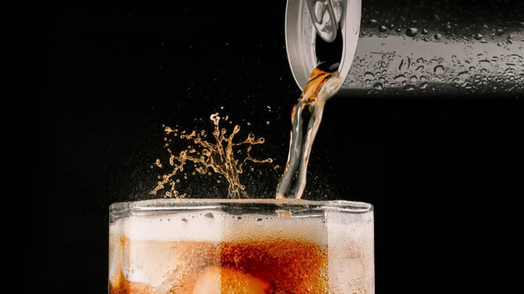 A soda being poured from a can into a glass filled with ice cubes, creating a splash. UAE Sugar Tax