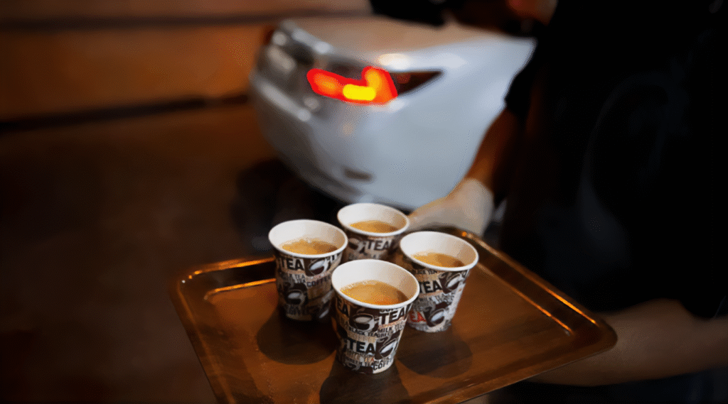 Late Night Food in Dubai: A person holding a tray with four paper cups of tea, with a blurred white car in the background at night.