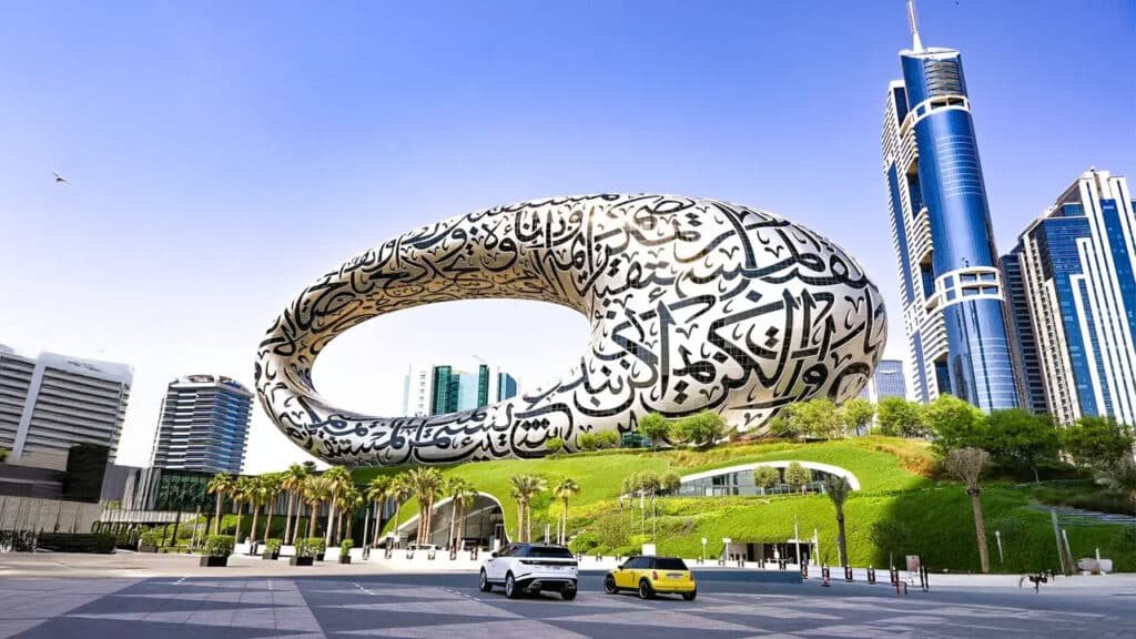 Tourist Spots in Dubai: A view of the Museum of the Future in Dubai, featuring its distinctive torus-shaped structure adorned with Arabic calligraphy, set against a backdrop of modern skyscrapers and a clear blue sky.