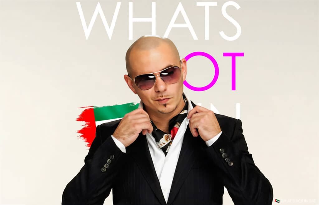 Global artist, Pitbull in a black suit and sunglasses adjusts his collar, standing in front of text saying What's Hot in UAE, and a stylized UAE flag design.
