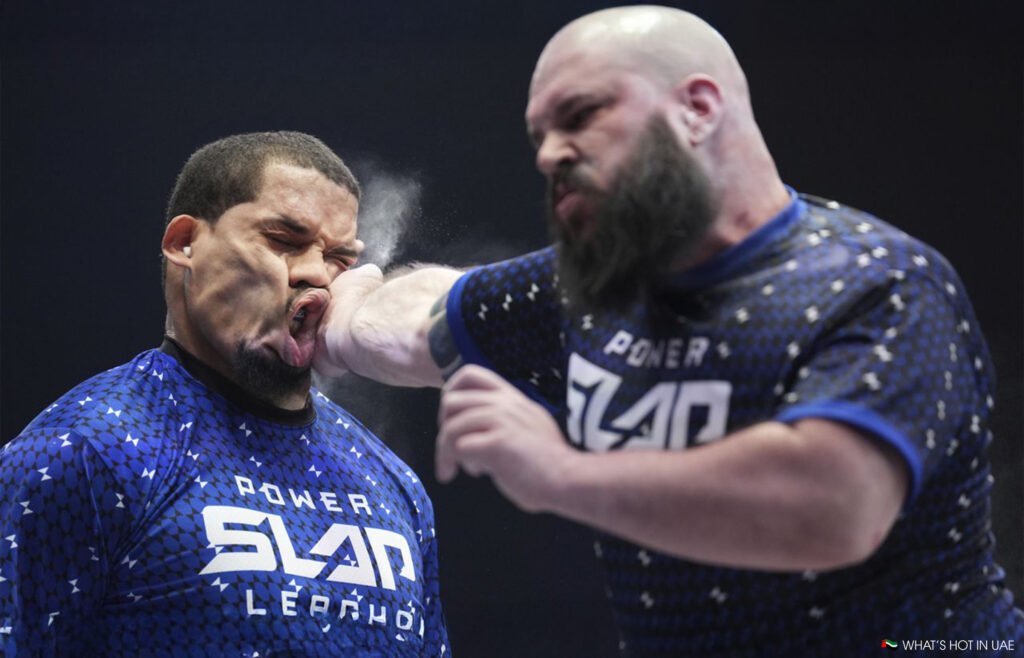 Power Slap UAE: Two men engaged in a slap-fighting competition, with one man slapping the other across the face, resulting in a dramatic facial distortion and a cloud of powder in the air.