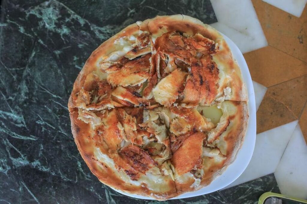 A pizza topped with grilled chicken pieces and cheese on a white plate, placed on a textured green and brown marble surface.