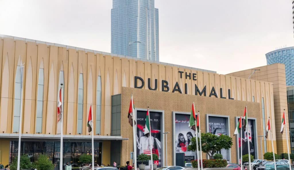 Front view of The Dubai Mall with flags and skyscrapers in the background on a cloudy day.