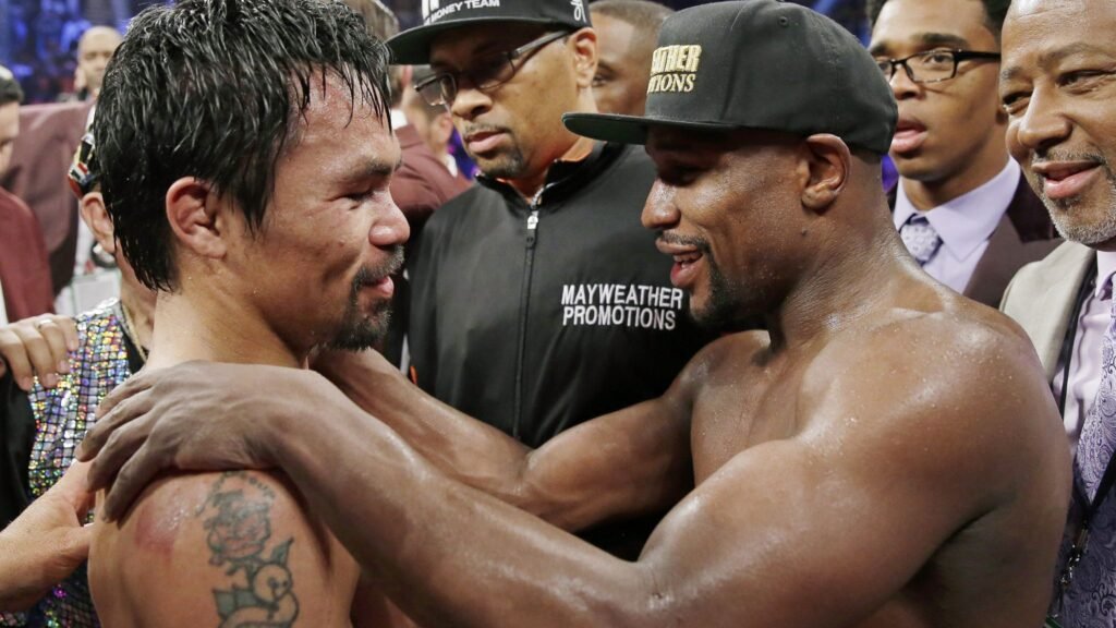 Pacquiao vs. Mayweather Rematch: Two boxers embracing in the ring after a fight, surrounded by people, with one wearing a "Mayweather Promotions" shirt.