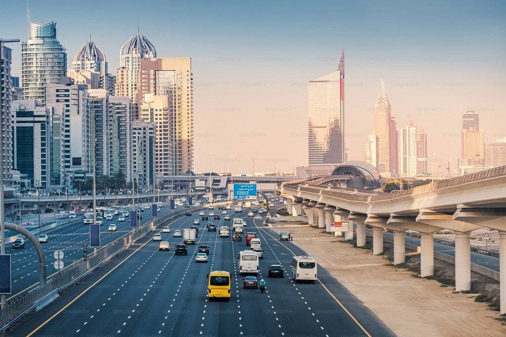 UAE traffic law: Urban highway with multiple lanes surrounded by tall skyscrapers and modern buildings under a clear sky.