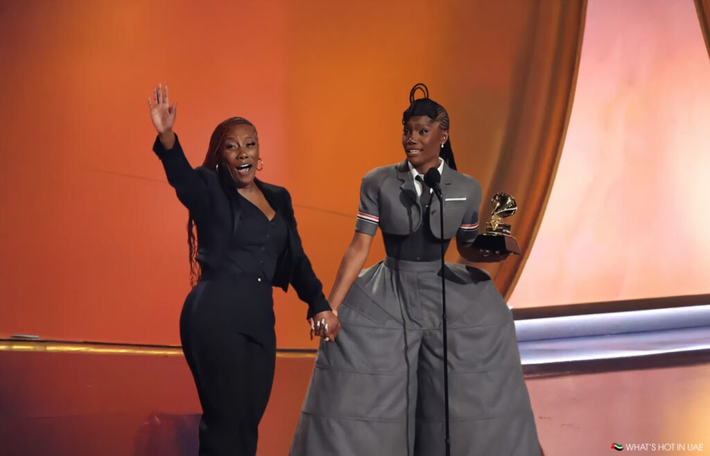 The 2025 Rap Drought: Doechii on stage, one holding a trophy and speaking into a microphone, while the other waves to the audience, with a colorful background.