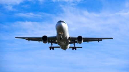 A commercial airplane flying overhead against a blue sky with scattered clouds.