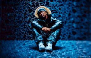 A person wearing a fur-lined hooded jacket and camo pants sits with crossed arms on a patterned blue floor and wall backdrop. The environment has a swirling blue pattern, creating a moody, abstract atmosphere.