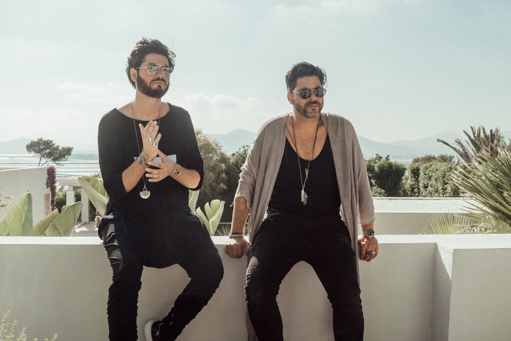 Ushuaïa Dubai NYE 2025: Birds of Mind wearing sunglasses sitting on a white wall outdoors, with plants and a scenic landscape in the background.