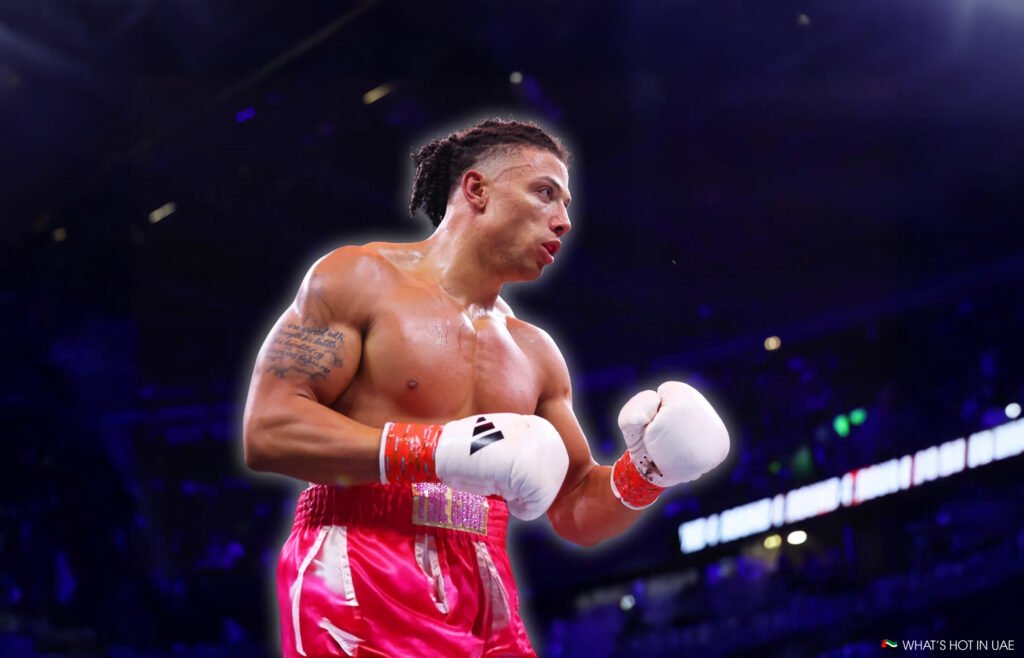 Chase DeMoor in the ring, wearing bright pink shorts and white boxing gloves, with cornrows and a muscular build, looks focused during a match under arena lights.
