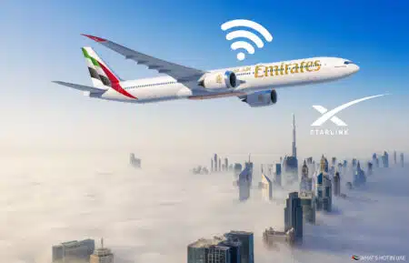 An Emirates airplane flying above a city obscured by clouds, with a WiFi symbol and Starlink logo, set against a backdrop of skyscrapers.