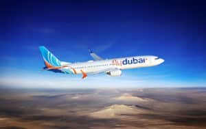 An airplane with 'flydubai' livery flying over a desert landscape under a clear blue sky.