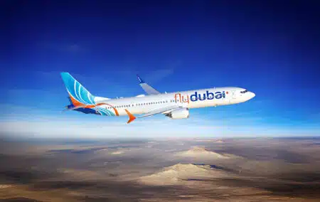 An airplane with 'flydubai' livery flying over a desert landscape under a clear blue sky.