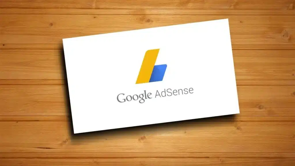 Google AdSense logo on a white card, set against a wooden background.
