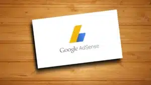 Google AdSense logo on a white card, set against a wooden background.