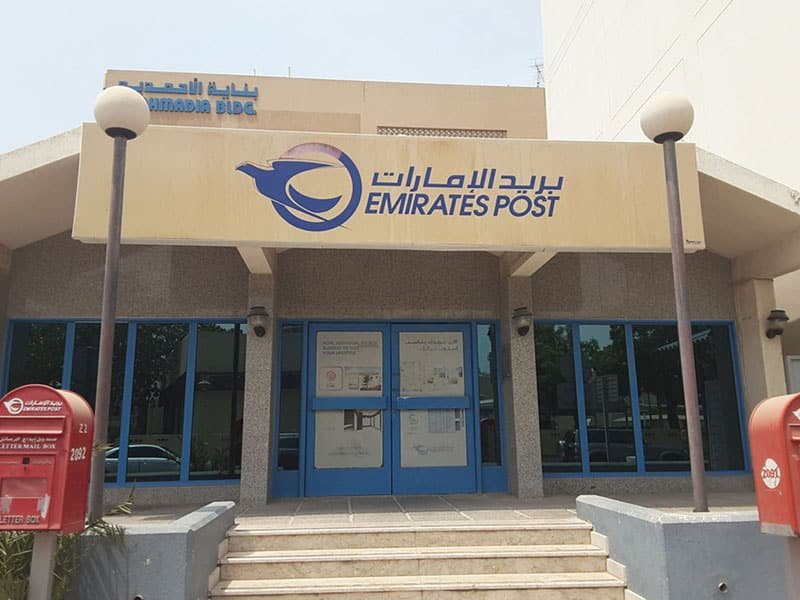 AdSense Verification UAE: Entrance of an Emirates Post office building with signage in English and Arabic, featuring mailboxes and glass doors.