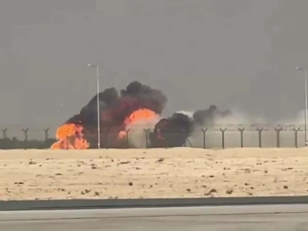 Indian Tejas Fighter Jet Crash. A large explosion with flames and thick black smoke rising behind a fence in a desert area near an airport runway.