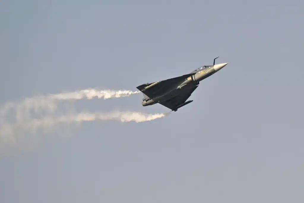 A fighter jet flying upward with contrails streaming behind it against a clear sky.