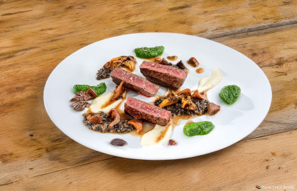A gourmet dish featuring medium-rare steak slices, sautéed mushrooms, and garnished with colorful sauces, elegantly plated on a white dish.