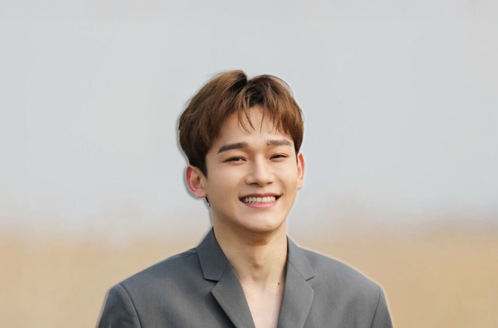 K-Pop in Dubai: Chen with short brown hair, wearing a gray suit, smiling at the camera.