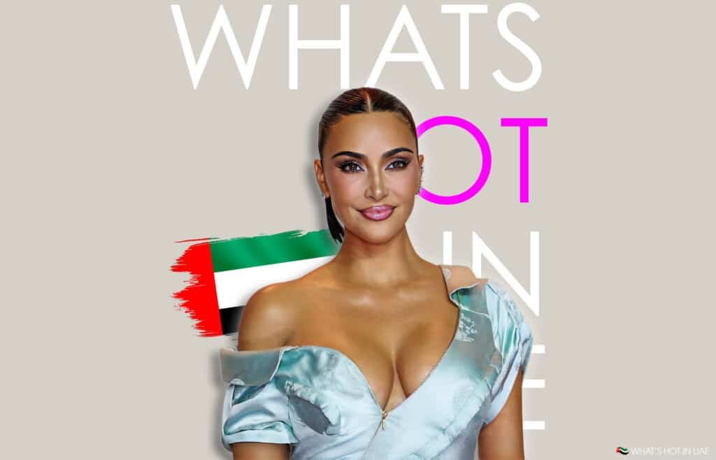 Kim Kardashian in an elegant blue off-the-shoulder dress stands in front of a digitally edited background featuring the phrase 'What's Hot in UAE' and a stylized UAE flag.
