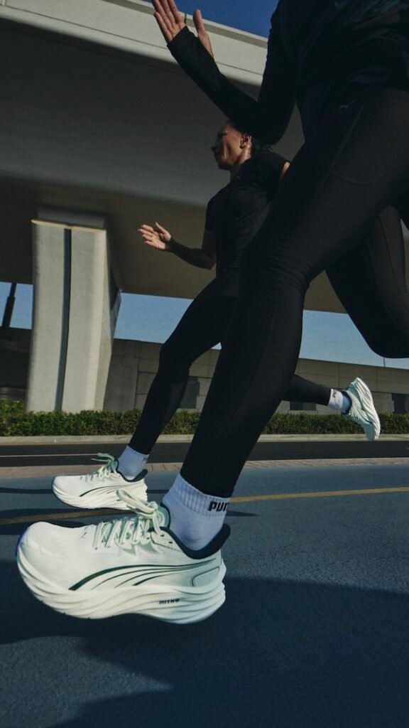 PUMA Running Dubai: Two people running on a road wearing white athletic shoes with green accents and black sportswear.